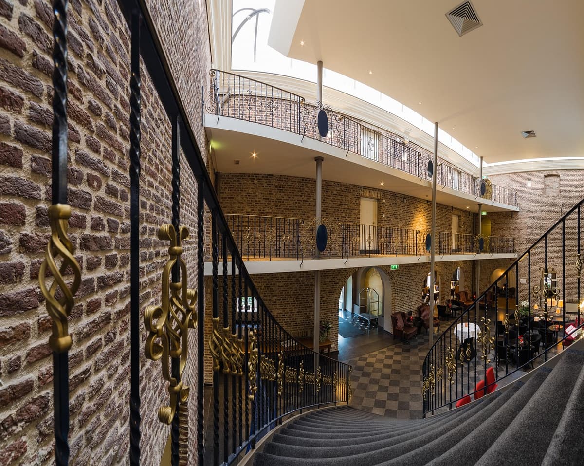 Elegante Hotel-Lobby mit hoher Decke, Wendeltreppe und Backsteinwänden in warmem Licht.