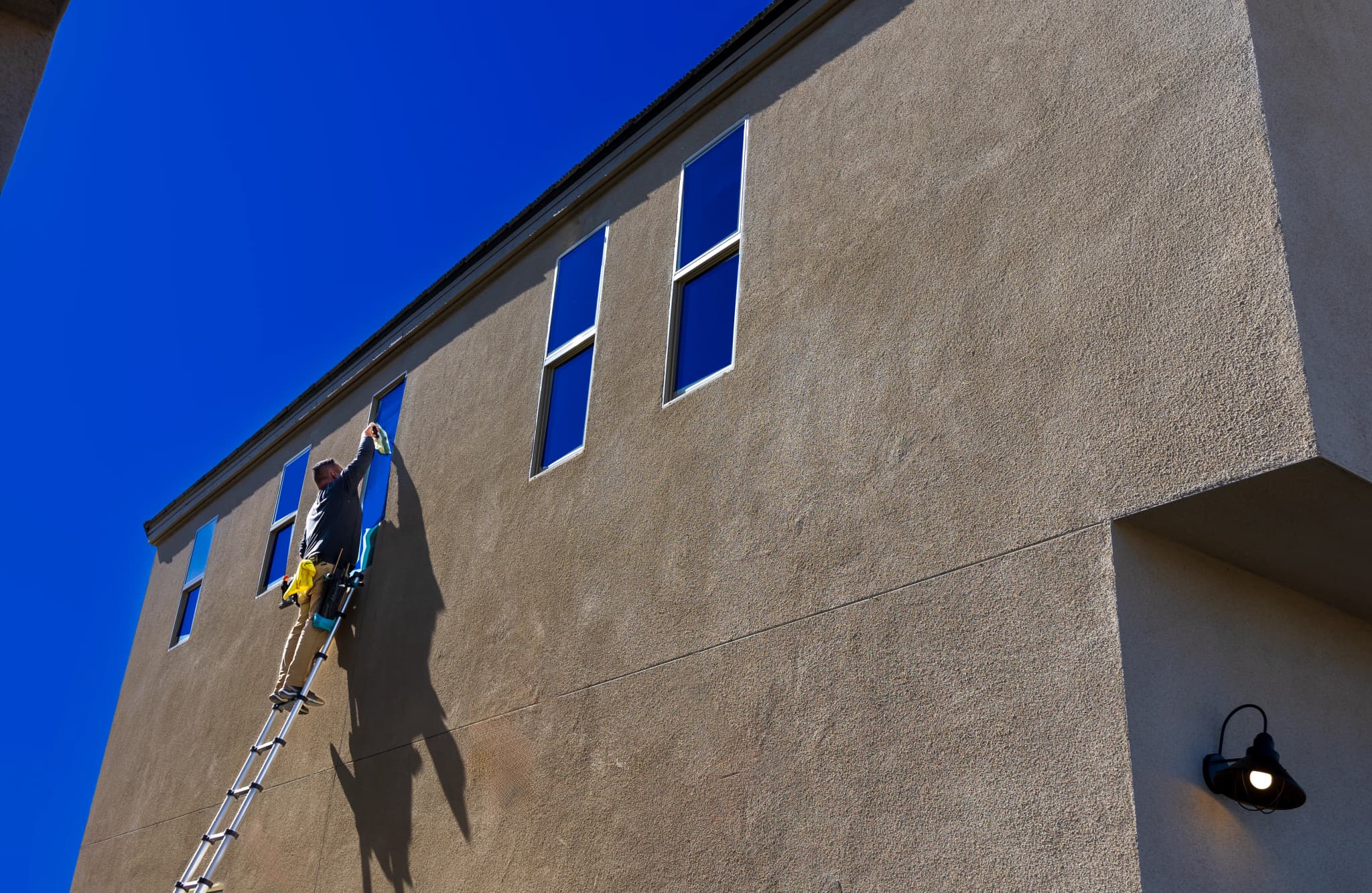 Handwerker reinigt auf einer Leiter die Fensterfassade eines mehrstöckigen Gebäudes