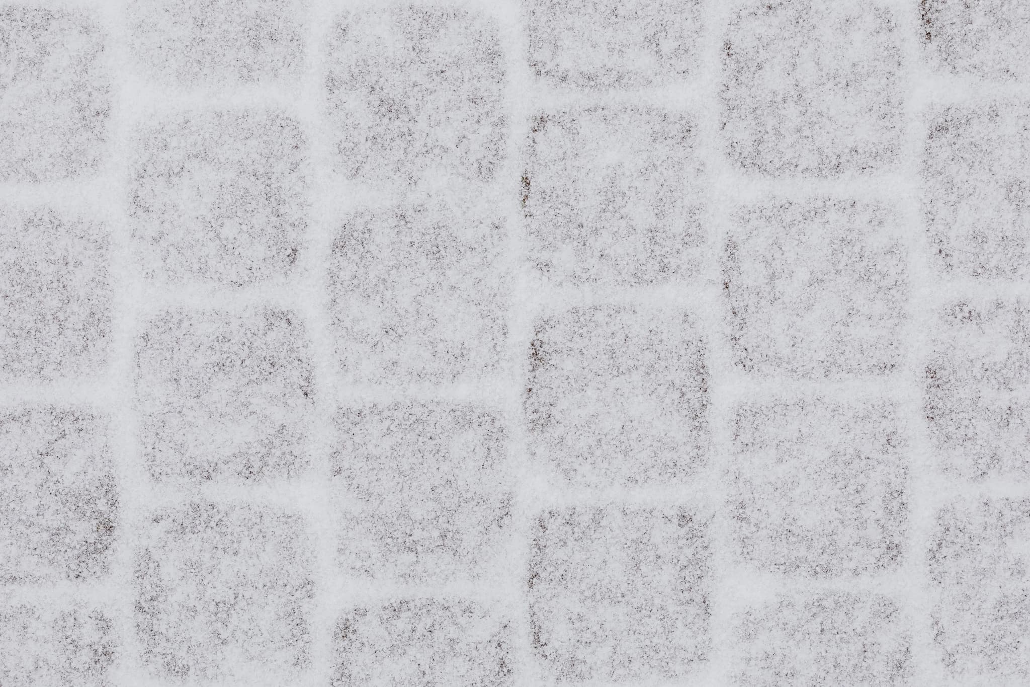 Schneebedecktes Pflaster mit quadratischem Fugenmuster im Winter aus der Vogelperspektive