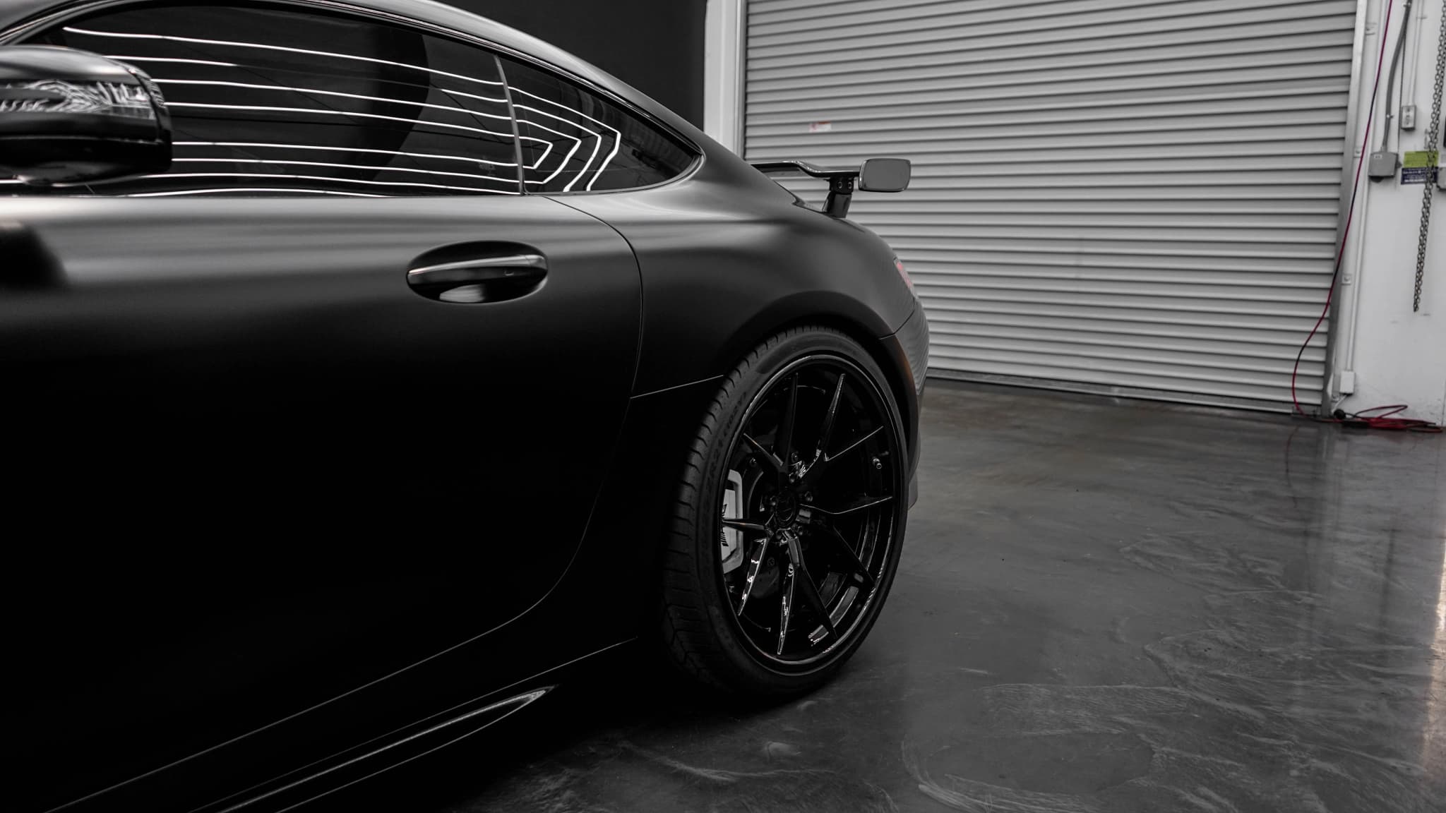 Schwarzes Auto in einer Garage mit Rolltor und glänzendem Betonboden