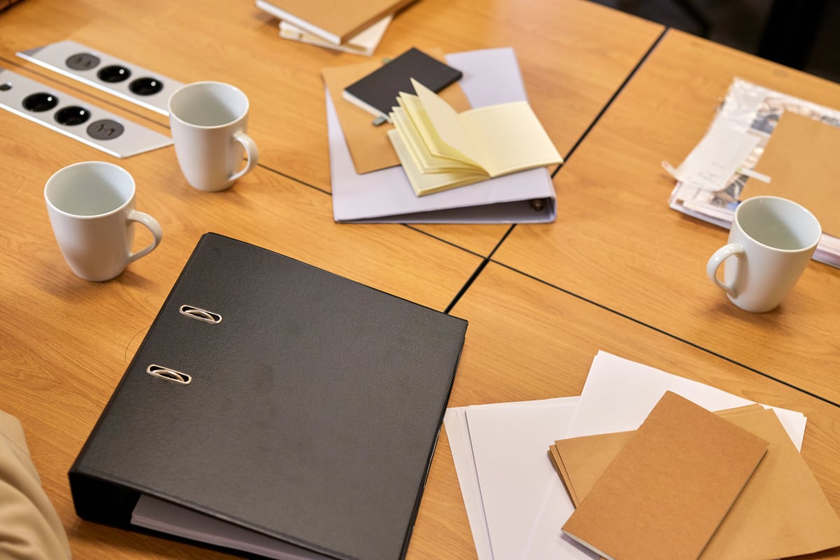 Schreibtisch in einem Büro mit Aktenordnern, Unterlagen und Tassen