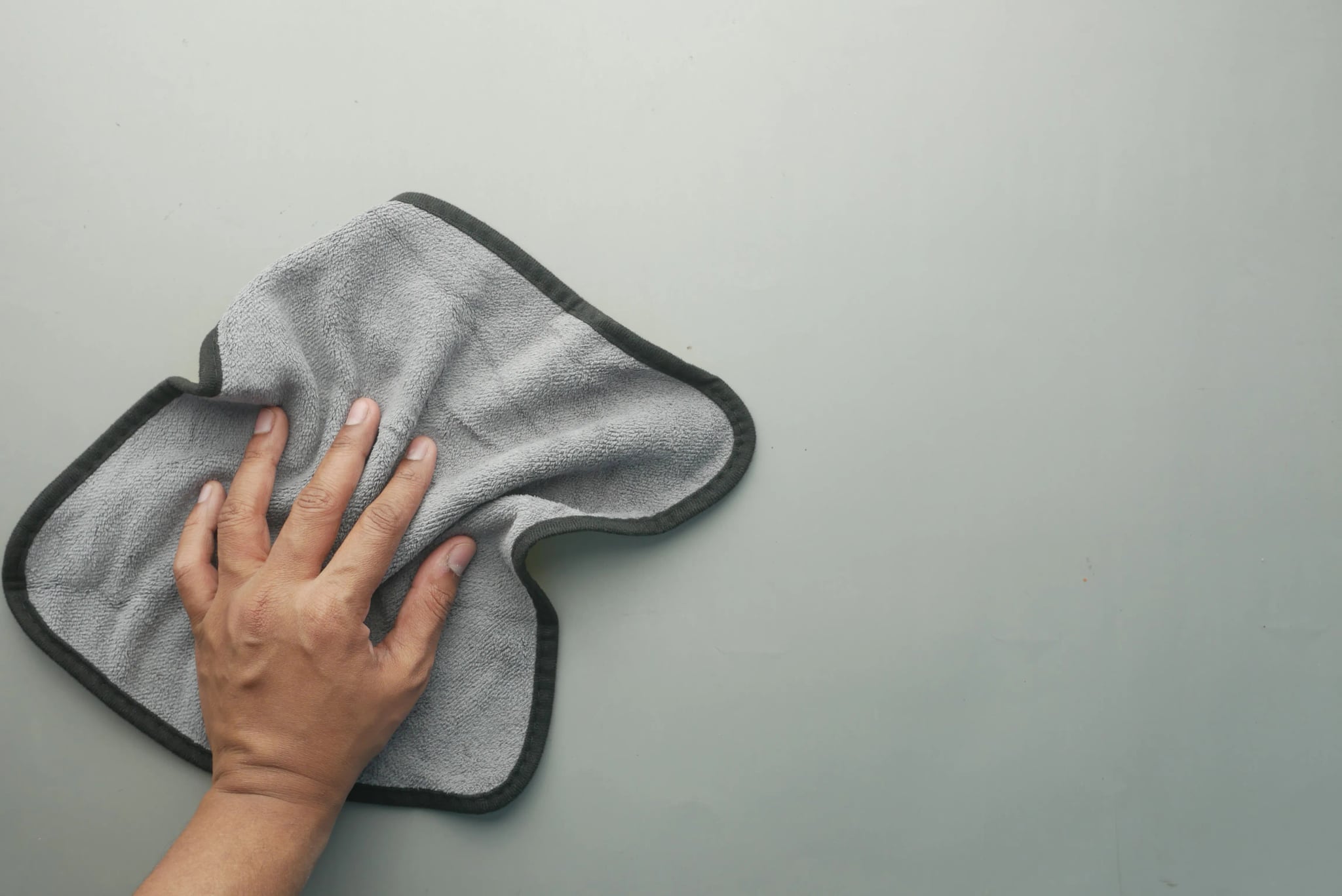 Hand wischt mit einem grauen Mikrofasertuch über einen hellen Tisch