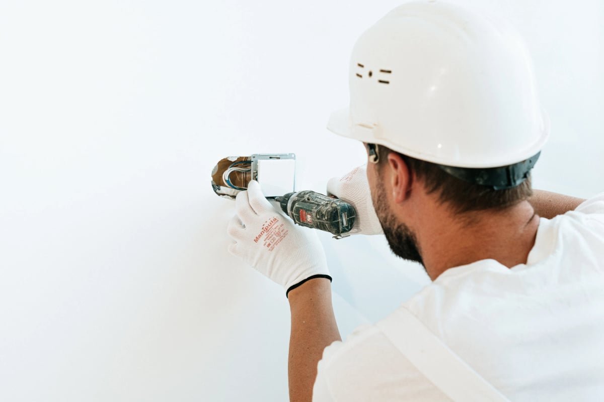 Handwerker mit Helm und Handschuhen arbeitet mit einem Werkzeug an einer Wand