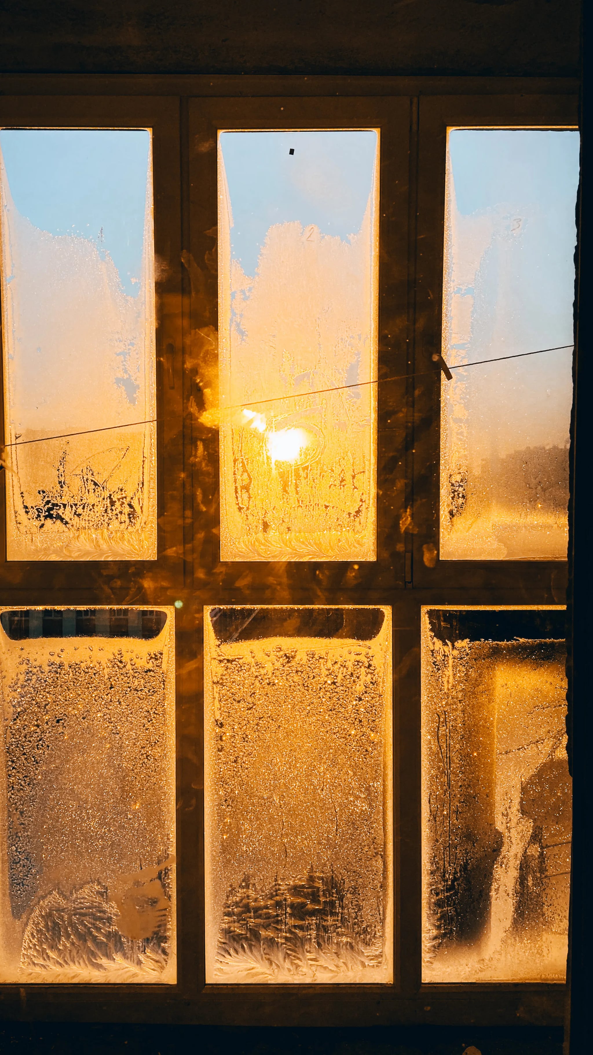 Gefrorenes Fenster mit Eiskristallen, durch das warmes Sonnenlicht scheint