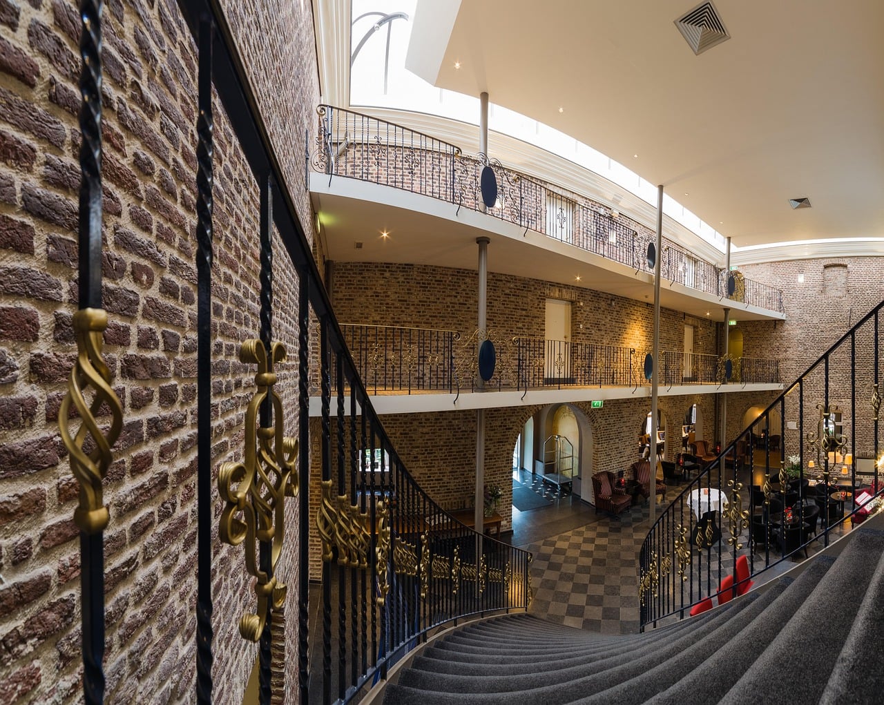 Elegante Hotel-Lobby mit hoher Decke, Wendeltreppe und Backsteinwänden in warmem Licht.